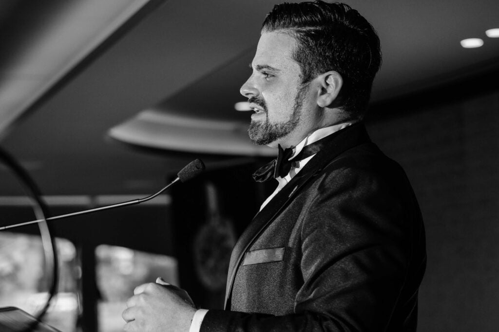 Man in a tuxedo standing at a podium in a formal setting