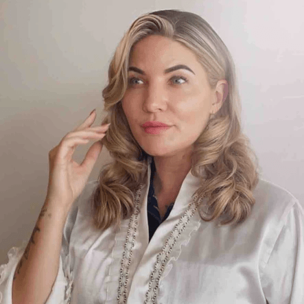 Woman with styled hair wearing a white outfit against a plain background