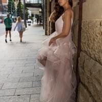 Woman in a white dress standing against a stone wall on a city street.