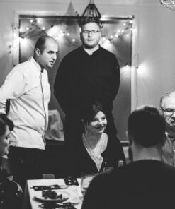 Black and white photo of a group of people in a social setting with a decorated wall in the background.
