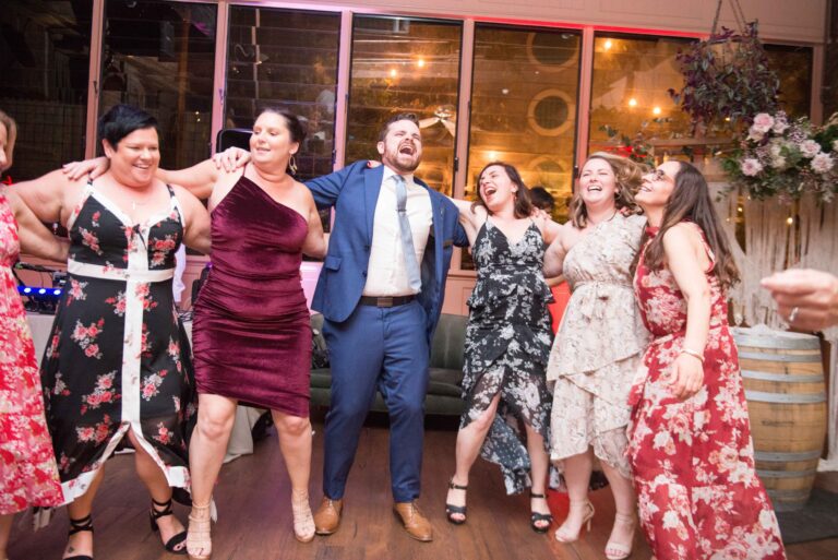 Group of people dancing together in a festive setting with decorations and a barrel in the background.
