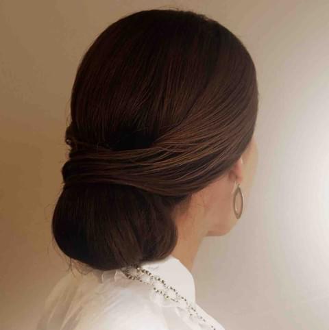 Woman with a stylish hair bun wearing a white top against a neutral background