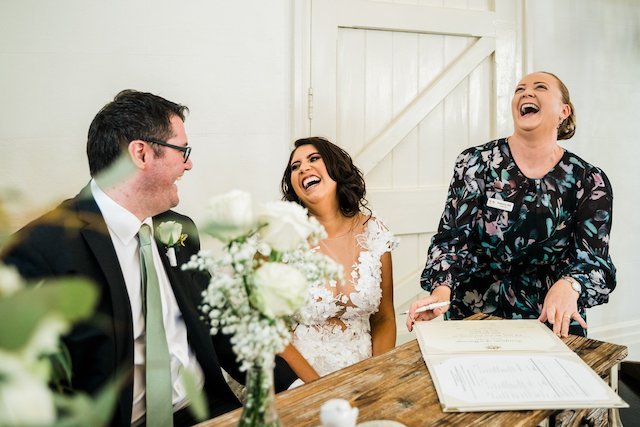 Wedding couple laughing with officiant at a table with wedding documents