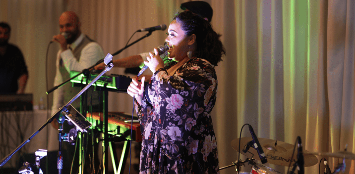 Woman singing into a microphone on stage with a band in the background