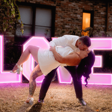 Couple embracing in front of a 'LOVE' sign with pink lighting.