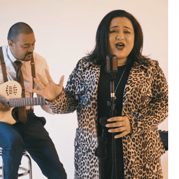 Man playing guitar and woman singing into microphone against a white background