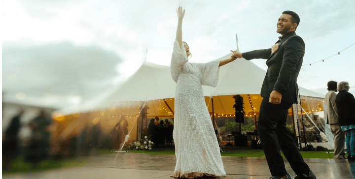 Two people dancing outdoors with a tented event in the background