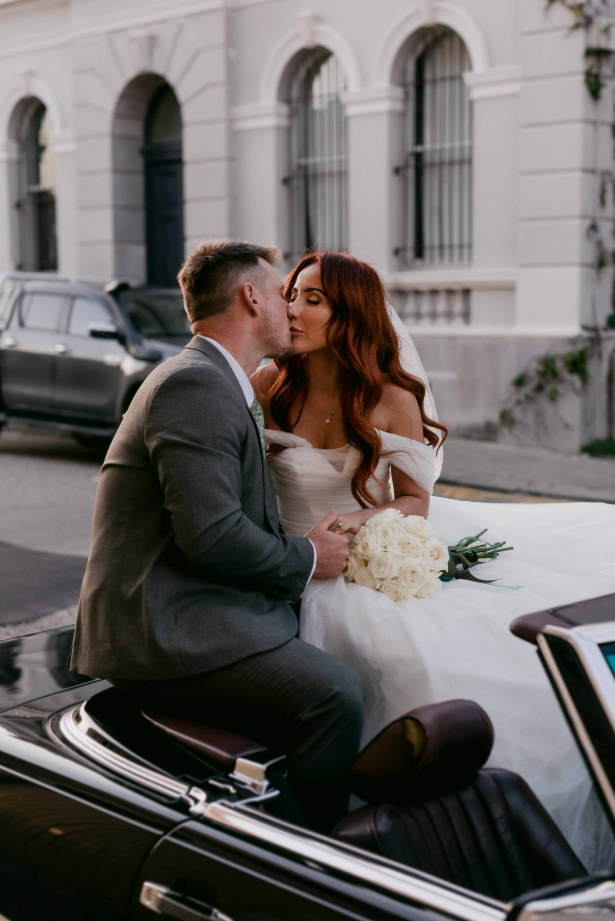 Couple sharing a kiss in front of a classical building.
