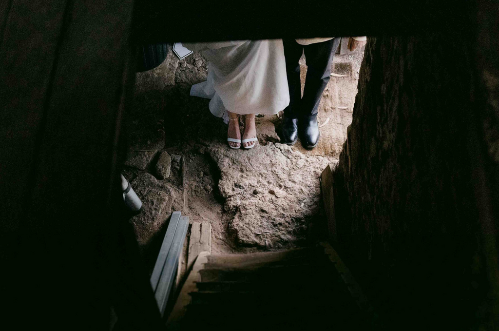 Two people standing on a stone path with a dark entrance or exit.