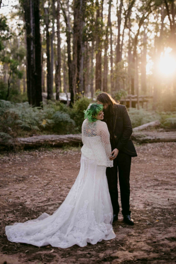 Couple in wedding attire standing in a forest with sunset light
