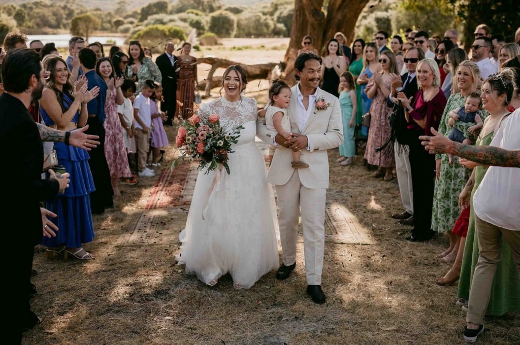 Wedding couple walking down the aisle with guests clapping outdoors.