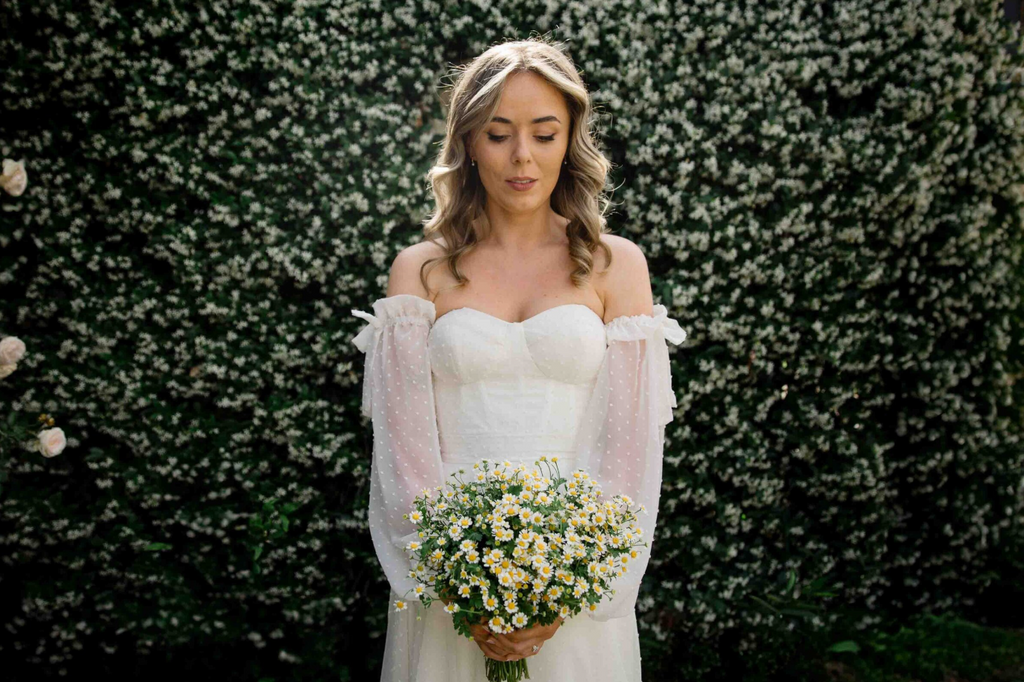Bride holding a bouquet of flowers against a green bush background
