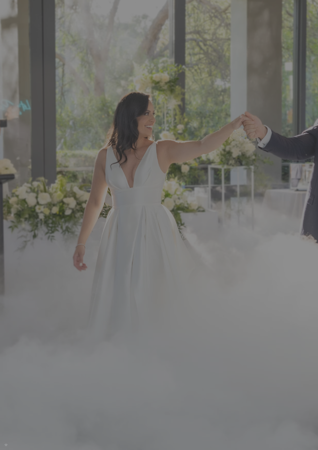 Couple in wedding attire walking hand-in-hand with a floral setup in the background