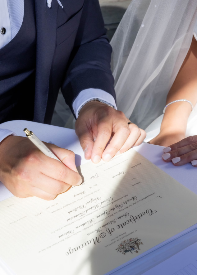 Two people signing a marriage certificate outdoors.