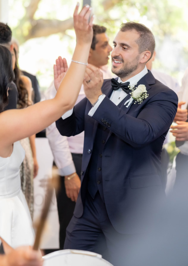 Groom in a navy suit with a floral boutonniere high-fiving a guest at a wedding.