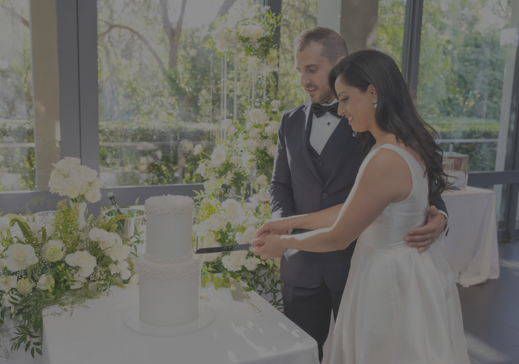Couple cutting a wedding cake in a decorated room with flowers and chairs.