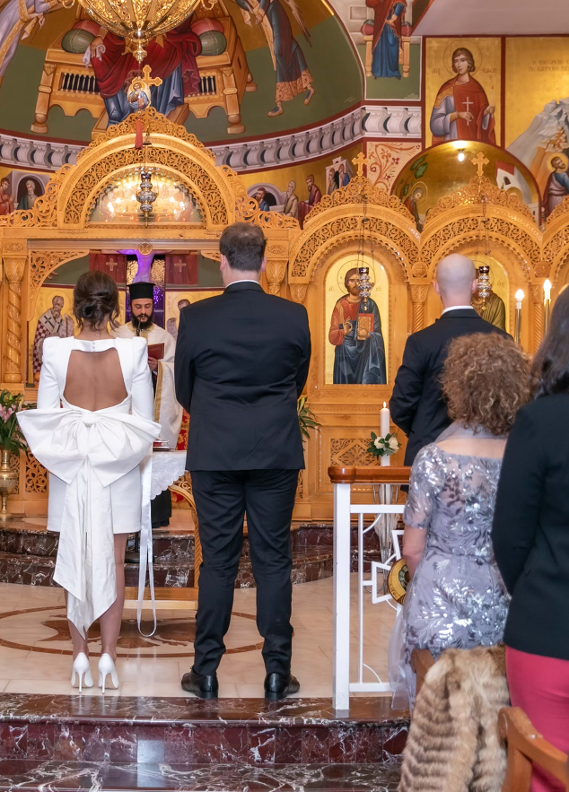 Group of people in formal attire in a decorated interior setting with religious iconography.