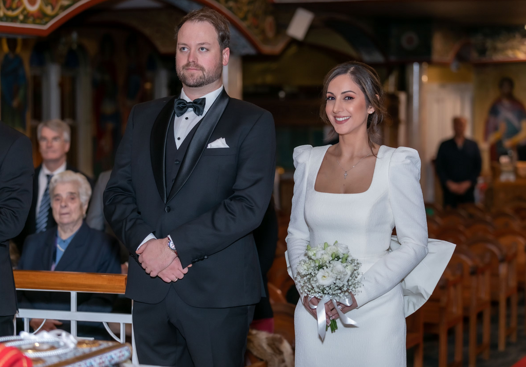 Man in a black suit and woman in a white dress standing together in an indoor setting.