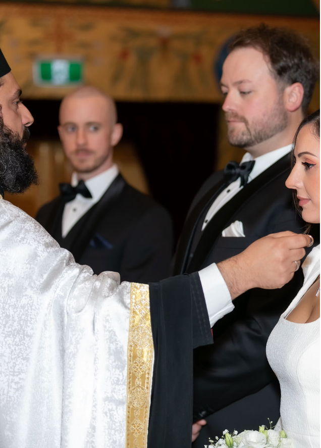 Man in a tuxedo adjusting a woman's dress with another man and woman in formal attire in the background.