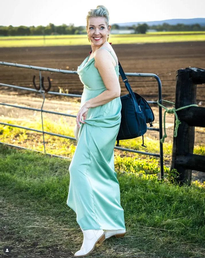 Woman in a light green dress standing in a field with a black cow and fence in the background.