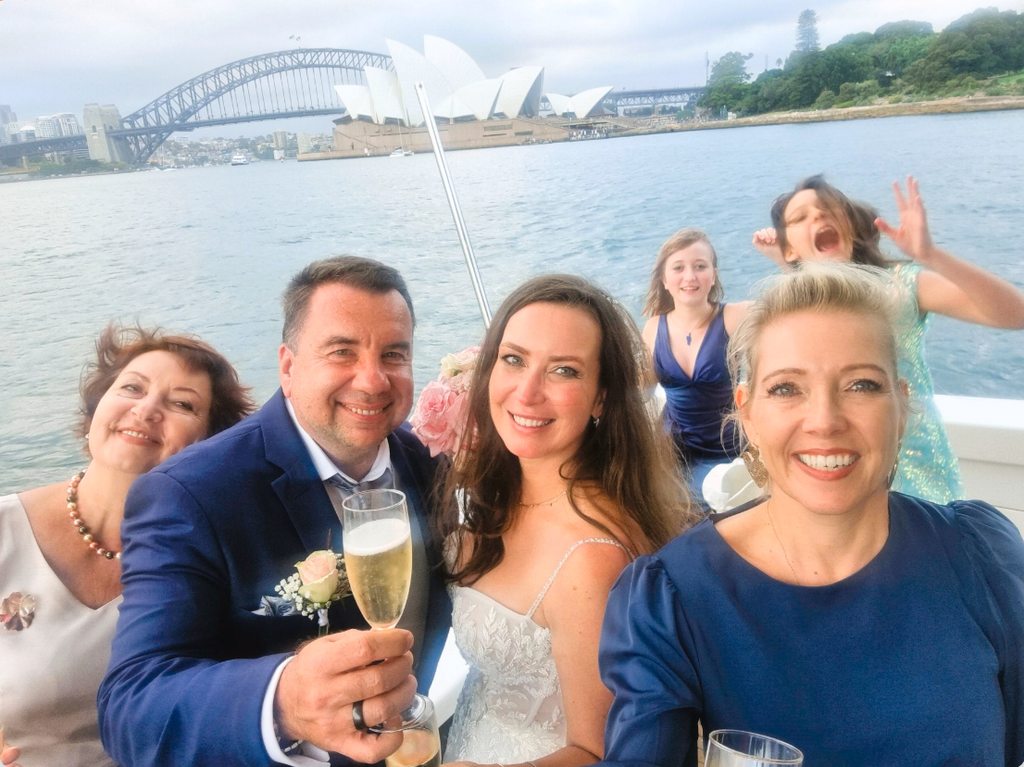 Group of people on a boat with a scenic background including a bridge and Opera House.