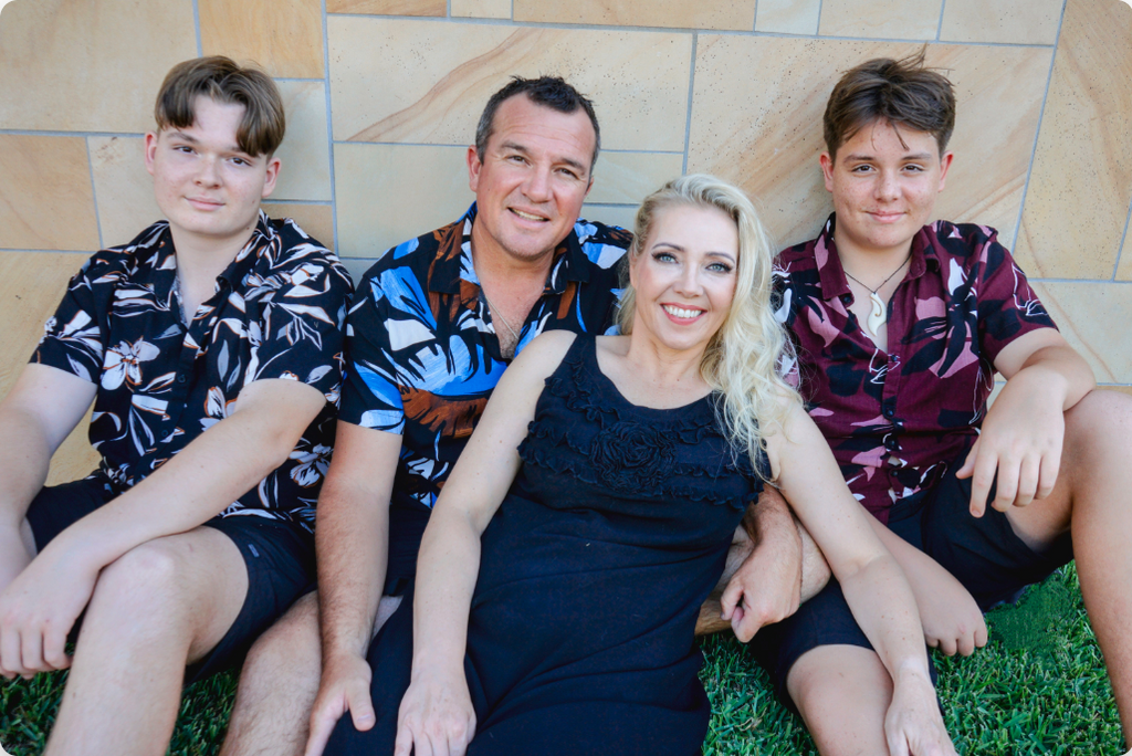 Family of four sitting on grass against a tiled wall