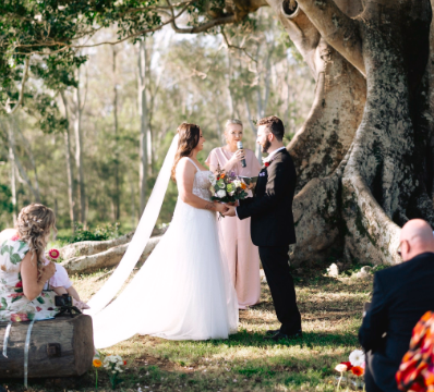Wedding ceremony taking place outdoors with a large tree in the background