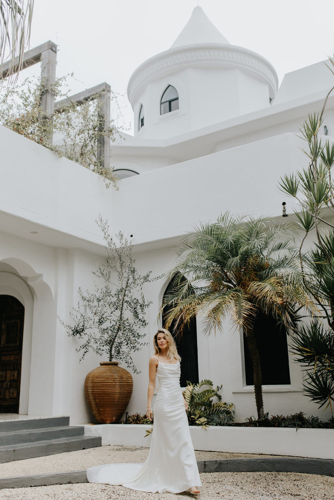 Woman in a white dress standing in front of a white architectural building with plants.