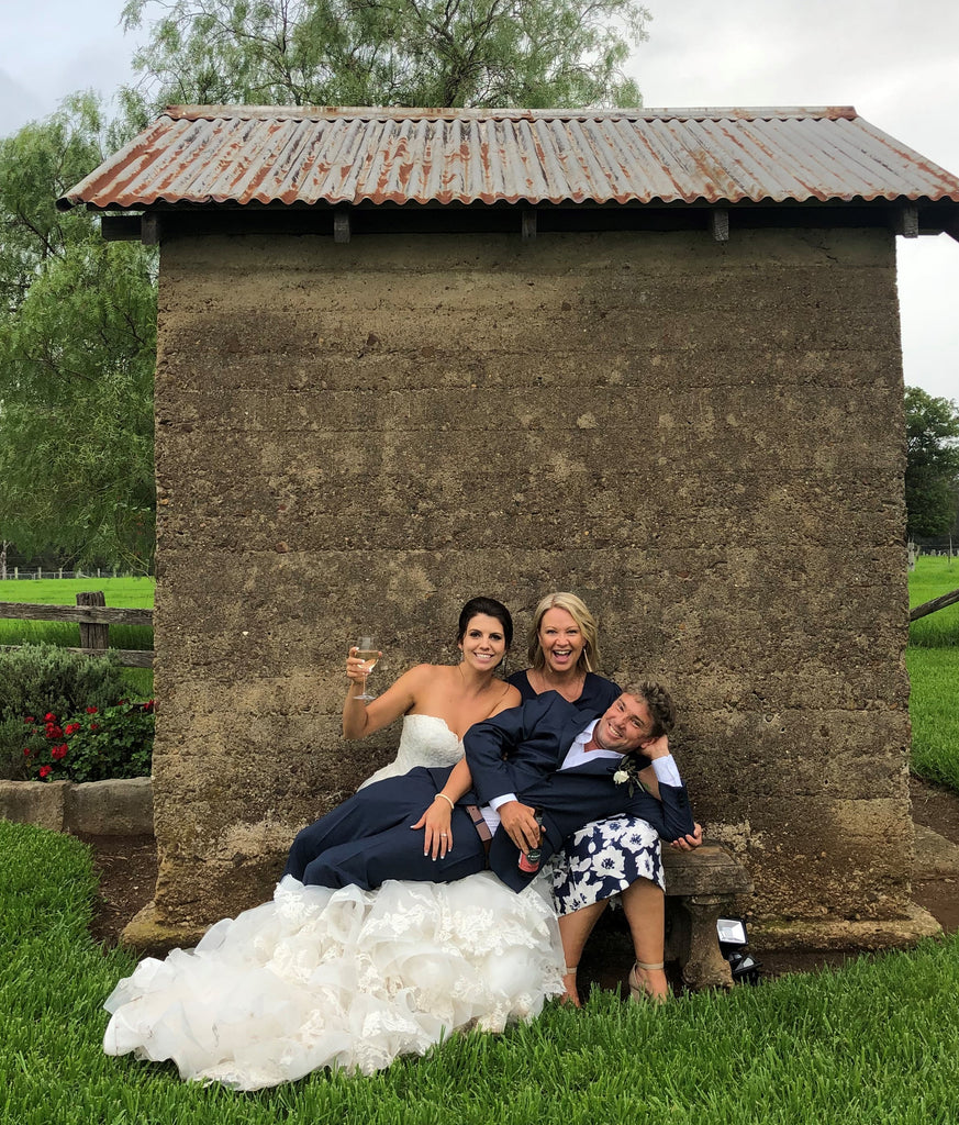 Three people posing in front of a rustic building with greenery in the background