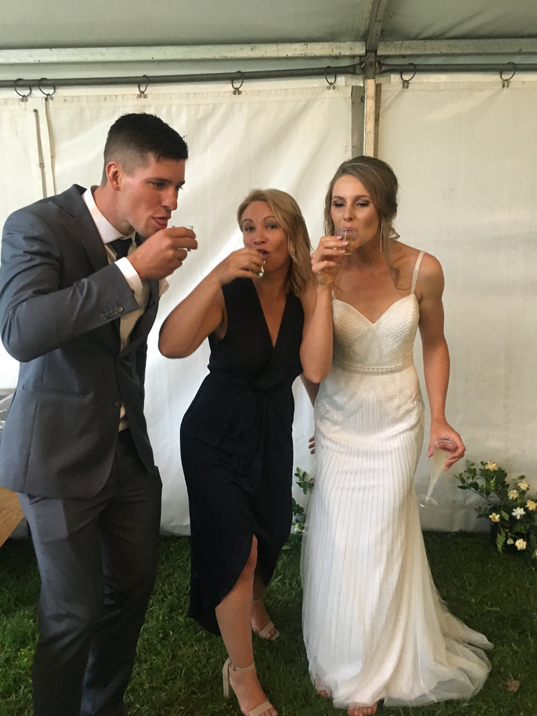 Three people, two of whom are in formal attire, standing under a white tent.