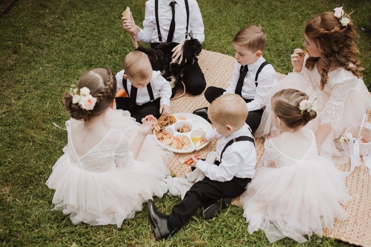 Children in formal attire sitting on a grassy area with a picnic setup.