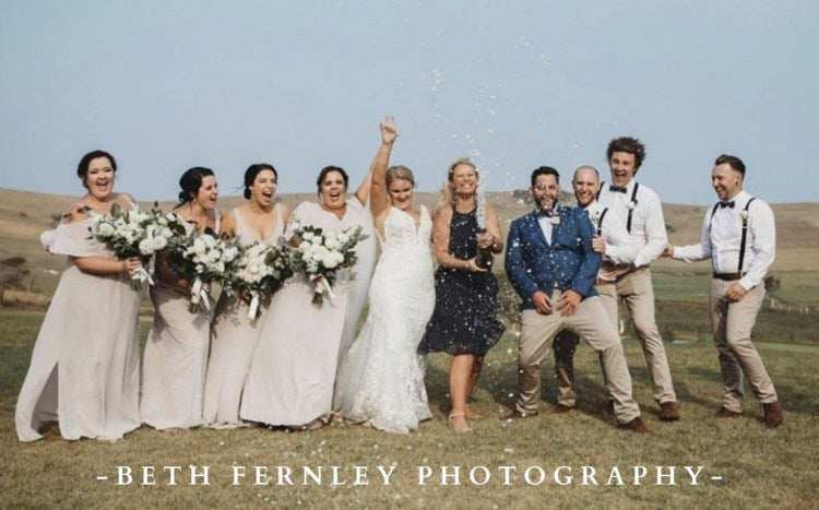 Wedding party celebrating outdoors with 'Beth Fernley Photography' watermark.